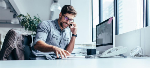 Image of a man talking on the phone in front of a computer in an office