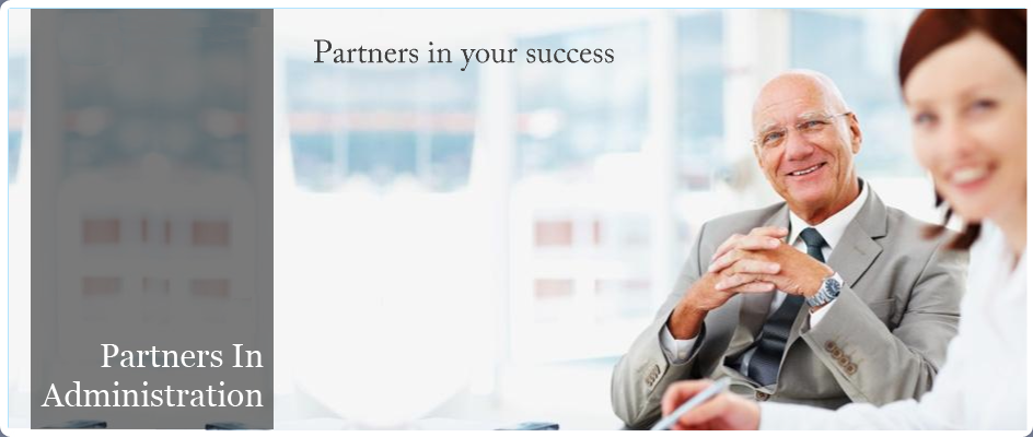 Partners in Administration, Partners in your success. Image of younger woman and older gentleman smiling sitting at a desk looking at the viewer.